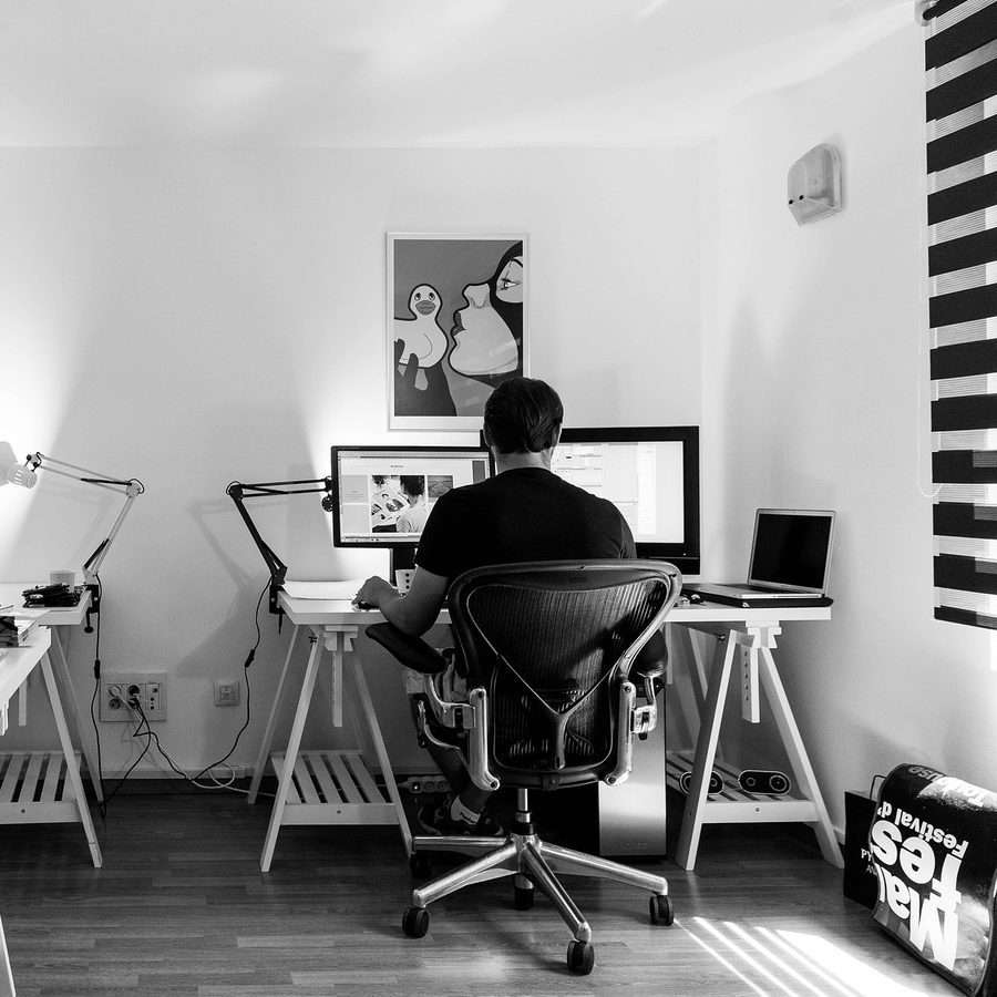 Une personne travaille devant deux écrans, dans un bureau lumineux